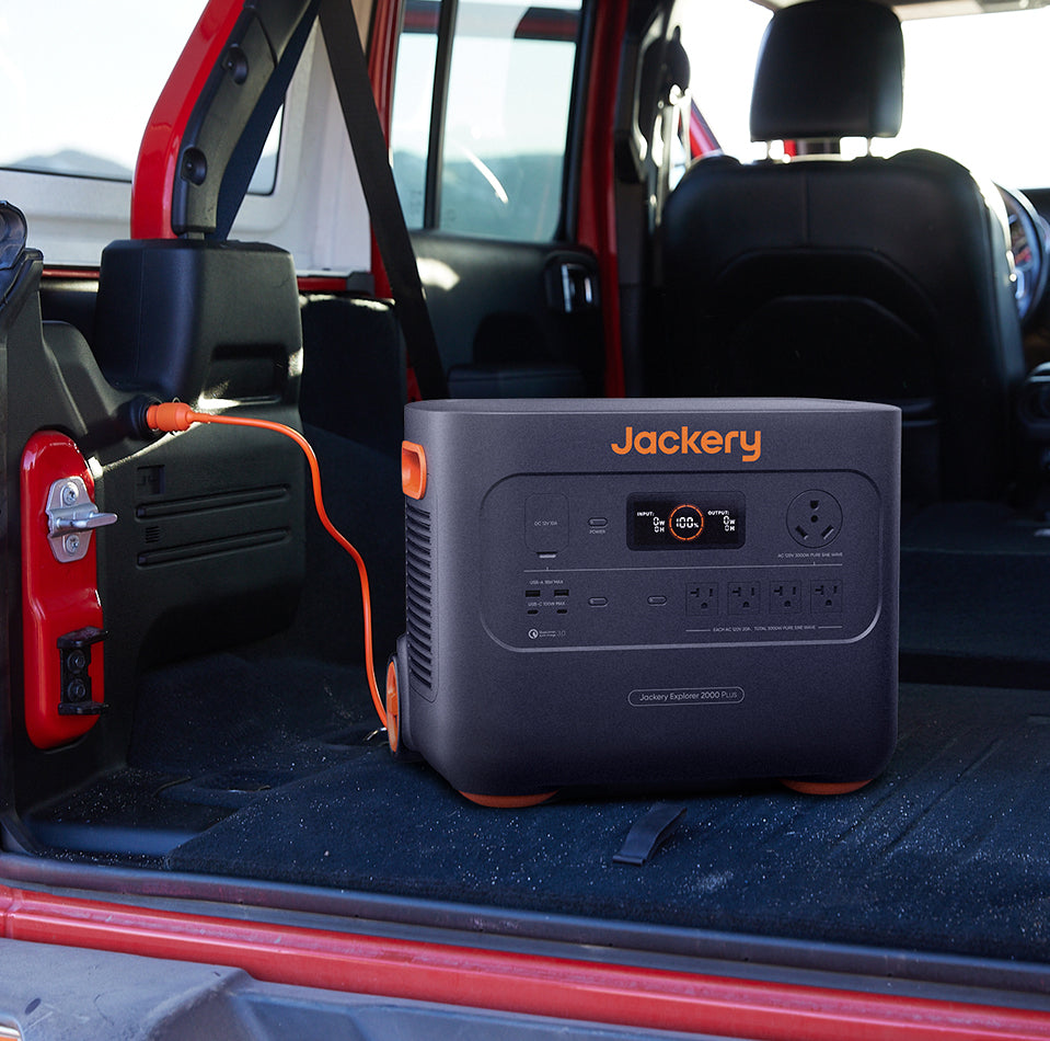 A red vehicle houses the Jackery Explorer 2000 Plus Portable Power Station, equipped with an advanced LiFePO4 battery. Connected via an orange cable, it offers multiple ports and has a digital display on the front.